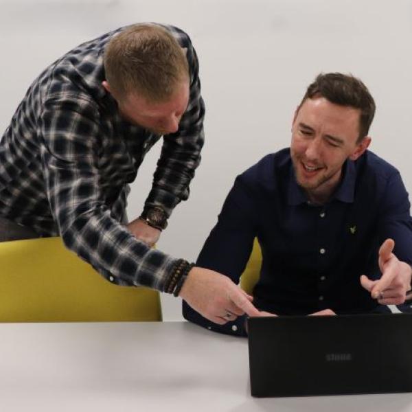 Two people talking whilst looking at a laptop in an office